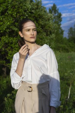 Trendy giyen güzel şık yasaktır kız gömlek, bej pantolon beyaz ve açık havada güneş ışığı tutar içinde peruk altında yeşil çayır onun elinde bir sigara kafes. Reklam tasarımı. Kopya alanı.