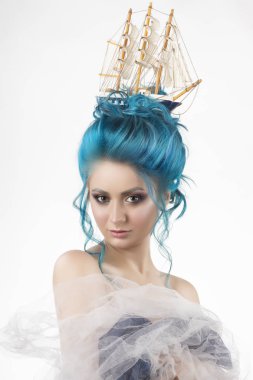 Sensual young girl with naked shoulders and painted blue hair stowed in an artistic hairdo with a toy sailboat in her hair, covering her chest with blue and white veils. Isolated in white. Copy space clipart