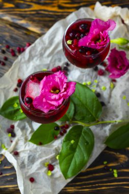 İki makara kırmızı bardak çilek, buz ve pembe çiçekler üzerinde tam hangi çilek ve yeşil tropikal yaprak vintage ahşap bir masa üzerinde bir dalı yalan Ambalaj Kağıt buruşuk. Kopya alanı.