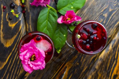 İki bardak kırmızı bardak çilek, buz ve hangi yalan çilek ve yeşil tropikal bir dalı bırakır vintage ahşap bir masa üzerinde bir pembe çiçekler ile dolu. Uzay kopyalayın. Ticari tasarım.