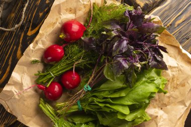 Demet maydanoz, dereotu, fesleğen taze otlar, turp ve kuzukulağı yalan bir plaka üzerinde bir ambalaj kağıdı eski bir ahşap masa kaplı. Uzay kopyalayın. Reklam tasarımı. Mutfak, Restoran, yemek