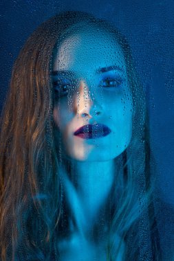 Sanat stil portre bir pencere cam arkasında bir yalnız güzel üzgün model kız mavi tonları, yağmur bitti düşer. Kavramsal, ticari ve moda tasarımı. Kopya alanı.