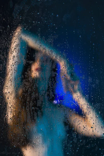 ガラスの後ろに立って美しい細い裸の女の子のぼやけたシルエットは水滴で覆われています ブルーの色調で芸術的 概念的な写真 コピー スペース — ストック写真