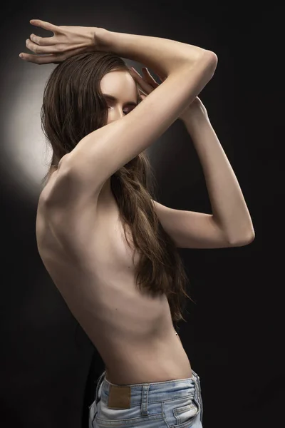 Beautiful slim flexible athletic topless girl model covers her naked breast with her hair on grey black gradient background. Healthy skin. Copy space. Advertising, commercial and conceptual design.