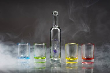 Beş çok renkli boş fondip bardakları ve küçük şişe simetrik bir tiyatro duman gri bir arka plan yerleştirilir. Kavramsal, ticari ve reklam fotoğraf. Kopya alanı.