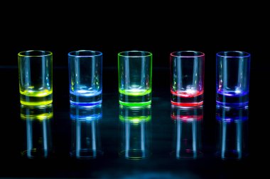 Beş çok renkli boş fondip bardakları bir cam yüzeye simetrik olarak yansıtan siyah bir arka plan yerleştirilir. Kavramsal, ticari ve reklam fotoğraf. Kopya alanı.