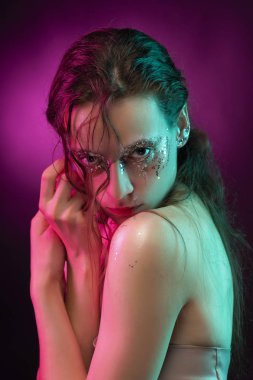 Yaratıcı makyaj ile güzel kız pembe ve mavi ışıkla aydınlatılmış yüzünde glitter gözyaşları ile yapılmış. Pembe bir arka plan. Kavramsal, reklam ve ticari tasarım. Kopya alanı.