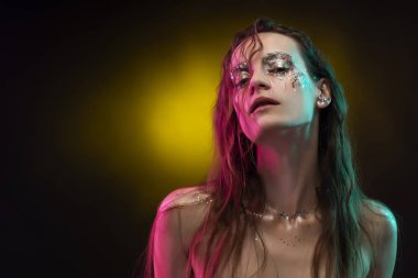 Yaratıcı makyaj ile güzel kız pembe ve mavi ışıkla aydınlatılmış yüzünde glitter gözyaşları ile yapılmış. Sarı arka plan. Kavramsal, reklam ve ticari tasarım. Kopya alanı.
