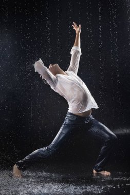 Anlamlı bir şekilde ıslak kot ve beyaz bir gömlek giymiş genç yalınayak biri modern dansları watersplashes arasında yağmurlu waterdrops altında su üzerinde dans ediyor. Siyah bir arka plan üzerinde izole. Kopya alanı.