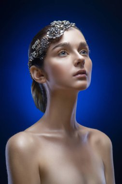 Güzel genç esmer model kızla çıplak omuz takı diadem mavi-siyah bir degrade arka plan üzerinde giyiyor. Altın makyaj. Sağlıklı temiz cilt. Uzay kopyalayın. Reklam ve konsept hazırlama.