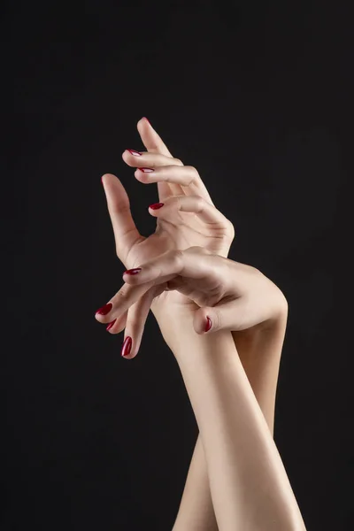 Closeup of beautiful woman hands with red manicure on the nails. Cream for palms, manicure and beauty treatment. Elegant and graceful arms with slender graceful fingers. Copy space. Isolated on black.