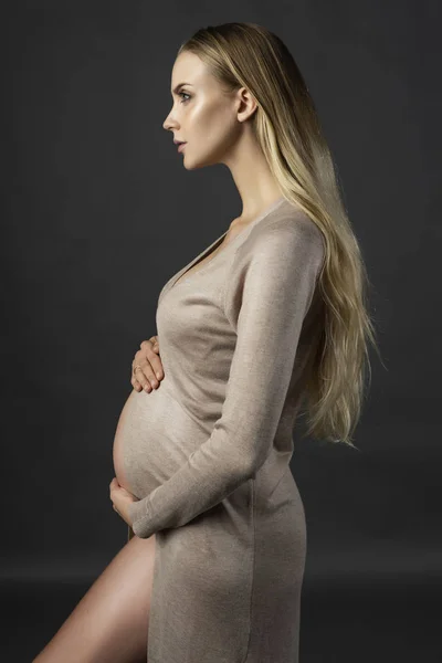 Güzel hamile genç kadın, bir iç çamaşırı ve örme elbise, geri alınan ve çıplak karnı Open'da usulca giymiş karnı elleri dokunur. Gri arka plan üzerinde profil fotoğrafı. Kopya alanı.