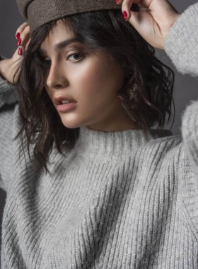 Rahat tarzı örgü sweaterputs başında gri arka plan üzerinde kap giyen güzel korkmuş esmer kız. Doğal çıplak makyaj. Moda, reklam tasarımı. Yakın çekim. Kopya alanı