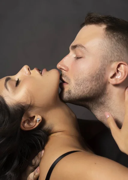 Güzel bir çift portre. Bir erkek sensually olan omuz çıplak bir kız çene dudaklarına dokunur. Rahat şık tarzı. Yaşam tarzı, moda, ticari tasarım. Gri arka planı.