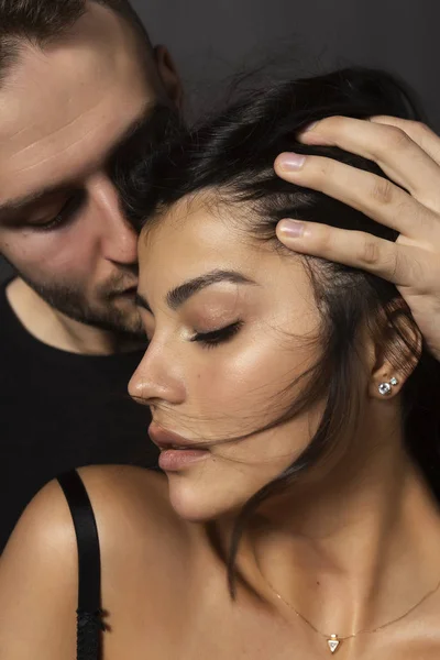 Güzel bir çift portre. Bir adam sensually dudaklarına olan omuz çıplak bir kız alnına dokunuyor. Rahat şık tarzı. Yaşam tarzı, moda, ticari tasarım. Gri arka planı.