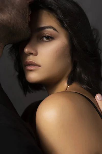 Güzel bir çift portre. Bir adam sensually dudaklarına olan omuz çıplak bir kız alnına dokunuyor. Rahat şık tarzı. Yaşam tarzı, moda, ticari tasarım. Gri arka planı.