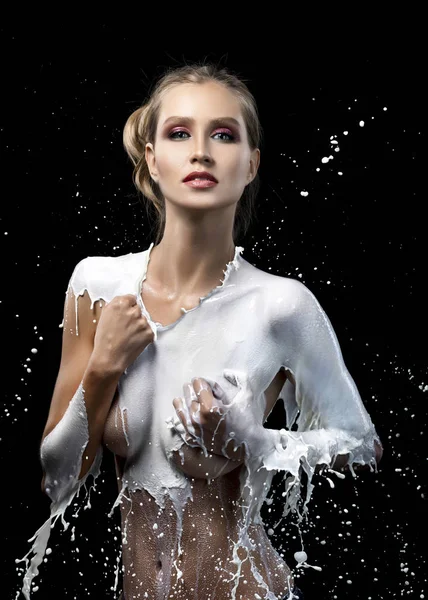 美しいブロンドの女の子は 水しぶきとミルクの滴から作られた服を着て 彼女の手で彼女の裸の大きな胸をカバーしています 黒の背景上に分離 ファッション 広告デザイン — ストック写真
