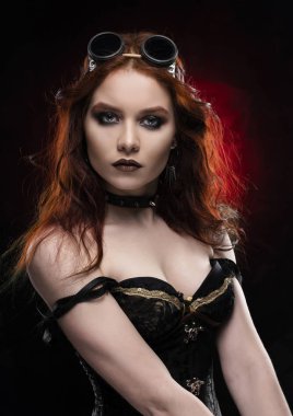 Kırmızı ve siyah arka plan üzerinde derin bir yaka içinde büyük bir meme ile Victorian tarzı steampunk kostüm giyen güzel gülümseyen Kızıl saçlı cosplayer kız. Portre. Kopya alanı.
