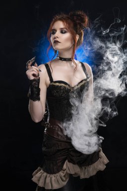 Düşünceli bir nefes duman siyah bir arka plan içinde derin bir bölünme ayakta büyük bir meme ile Victorian tarzı steampunk kostüm giyen güzel kızıl saçlı cosplayer kız. Kopya alanı.