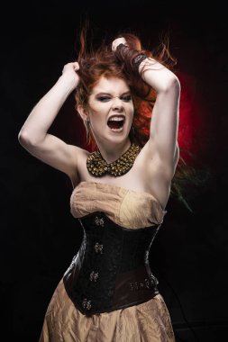 Victorian tarzı steampunk elbise çığlıklar ve shooks saçlarını elleri giyen güzel kızıl saçlı cosplayer kız. Kırmızı ve siyah arka plan. Kopya alanı.
