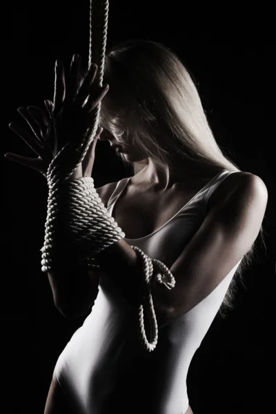 Büyük meme ve meme uçlarını kıyafet görünen güzel ince sarışın kız beyaz bir bodisuit giyen sensually ipleri siyah ile oynuyor. Sanatsal noir siluet fotoğraf. Kopya alanı.