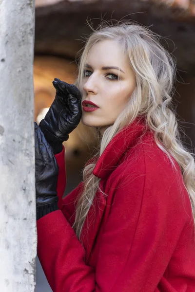 Egy gyönyörű szőke lány visel piros kabátot és kesztyűt áll — Stock Fotó