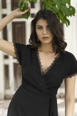 Güzel esmer kız, derin bir boyunlu siyah bir elbise giyiyor