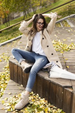 Açık renk pelerin, kot pantolon ve cam takan güzel bir kız.