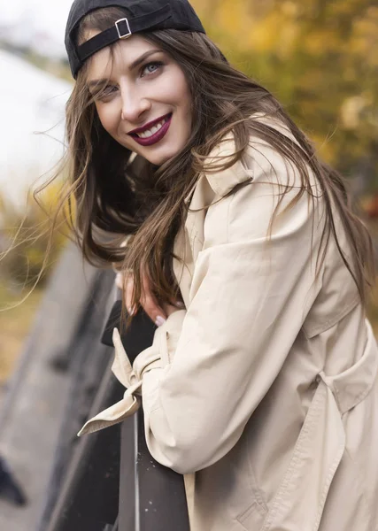 Egy gyönyörű, mosolygós lány, könnyű kabátban, farmerban és bazebben. — Stock Fotó