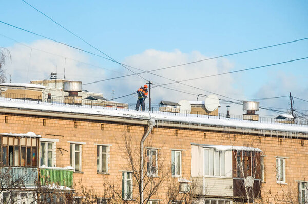 The janitor in uniform cleans snow after snowstorm from the roof of a multi-storey building in the city