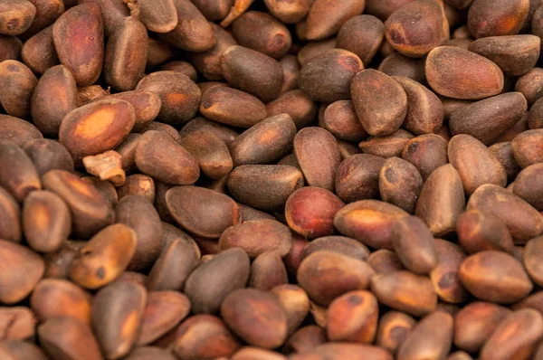 Uncleaned pine nuts in a brown shell lie mixed up closeup