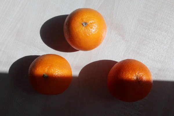 シャープな影と明るい朝の太陽に照らされた三角形の形の木のテーブルに横に 個のオレンジ — ストック写真
