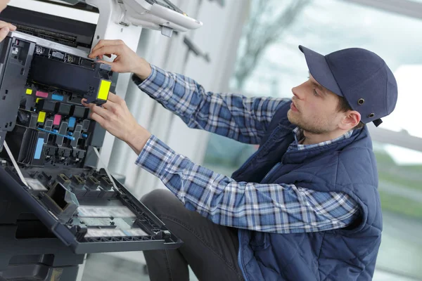 Jovem técnico ajustinf e configuração de uma impressora — Fotografia de Stock