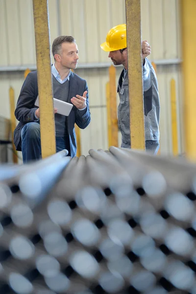 Двоє чоловіків-робітників обговорюють стопки труб — стокове фото