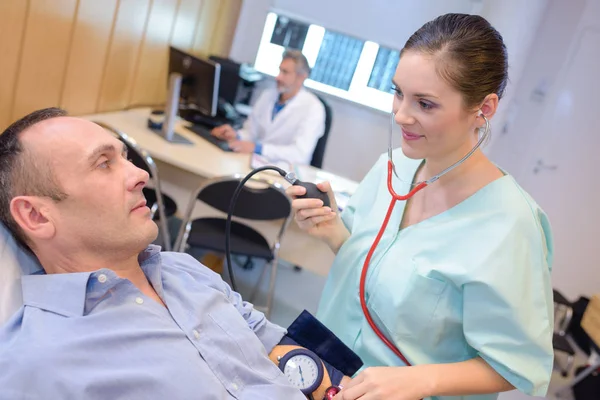 Enfermera tomando la presión arterial del hombre — Foto de Stock