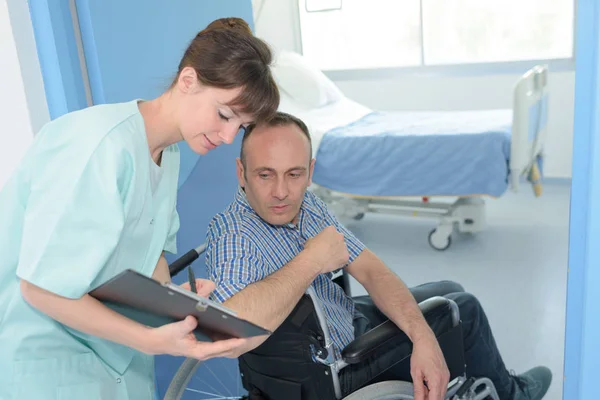 Man in wheelchair in hospital with a nurse with clipboard — Stock Photo, Image