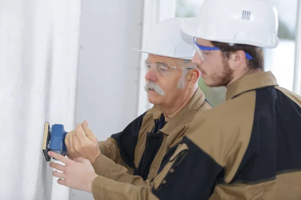 Aprendiz macho construtor lixar parede dentro de casa — Fotografia de Stock