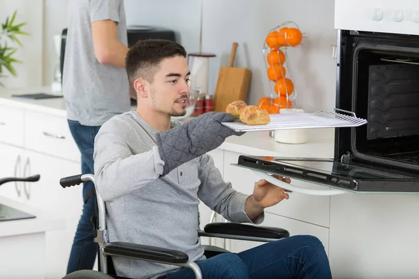 Jonge gehandicapte man op rolstoel zet gebak in de oven — Stockfoto