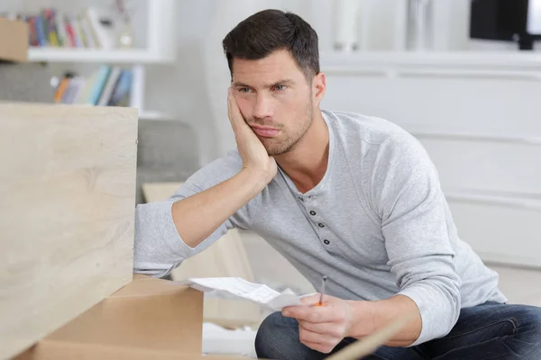 Frustrated man holding instructions for assembling furniture — Stock Photo, Image