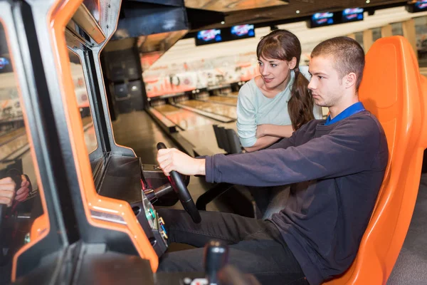 Young coupple playing driving wheel video game in game room — Stock Photo, Image