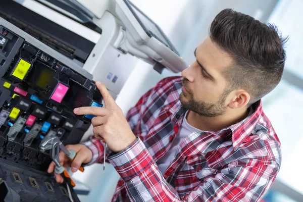 Jovem técnico do sexo masculino reparando máquina fotocopiadora digital — Fotografia de Stock