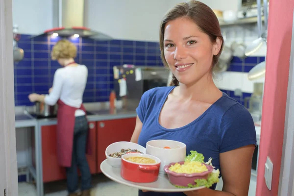 Waitress showing dishes to the camera and chef in background — Stock Photo, Image