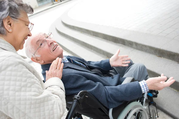 Senior kobieta pchanie męża niepełnosprawnych na ulicy — Zdjęcie stockowe