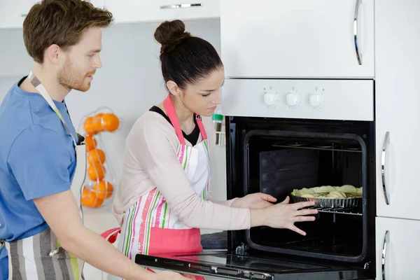 Feliz pareja cocinar pastel en el horno en casa —  Fotos de Stock