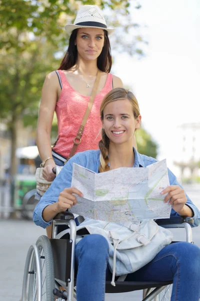 Två vänner besöker främmande stad en sitter i rullstol — Stockfoto