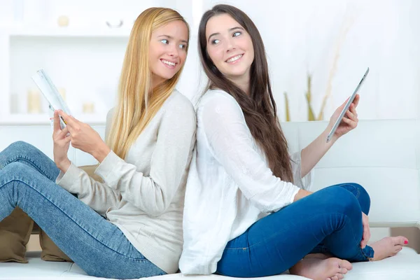 Young ladies using tablets, sat back to back — Stock Photo, Image