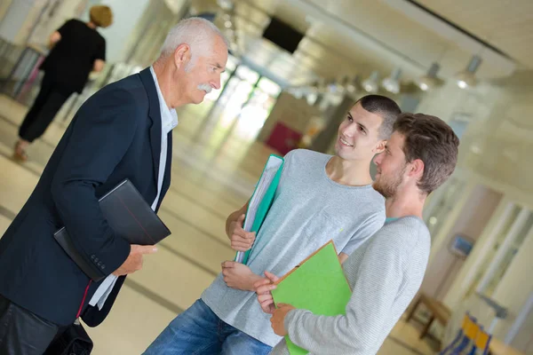 Ledande lärare diskuterar med eleverna i universitet korridor — Stockfoto