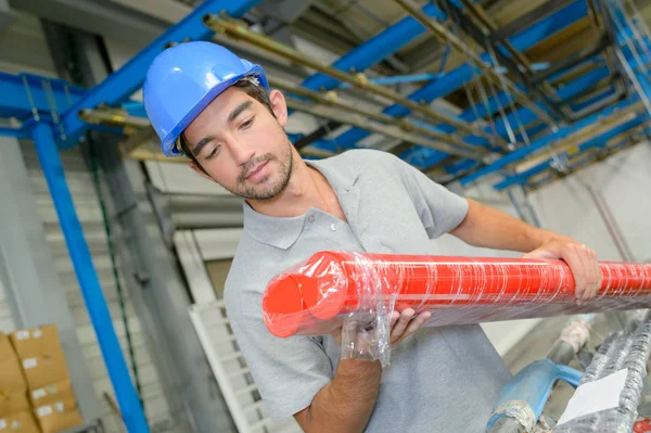 Trabalhador masculino olhando para longos tubos laranja — Fotografia de Stock