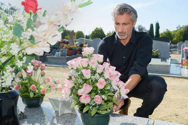 Homem colocando flores frescas no cemitério — Fotografia de Stock