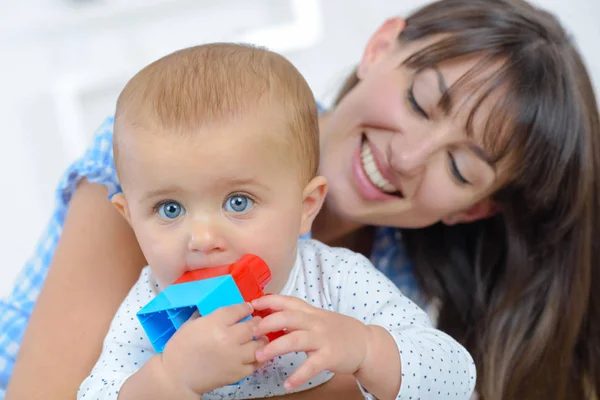 Mãe sorrindo para bebê mastigar brinquedo — Fotografia de Stock